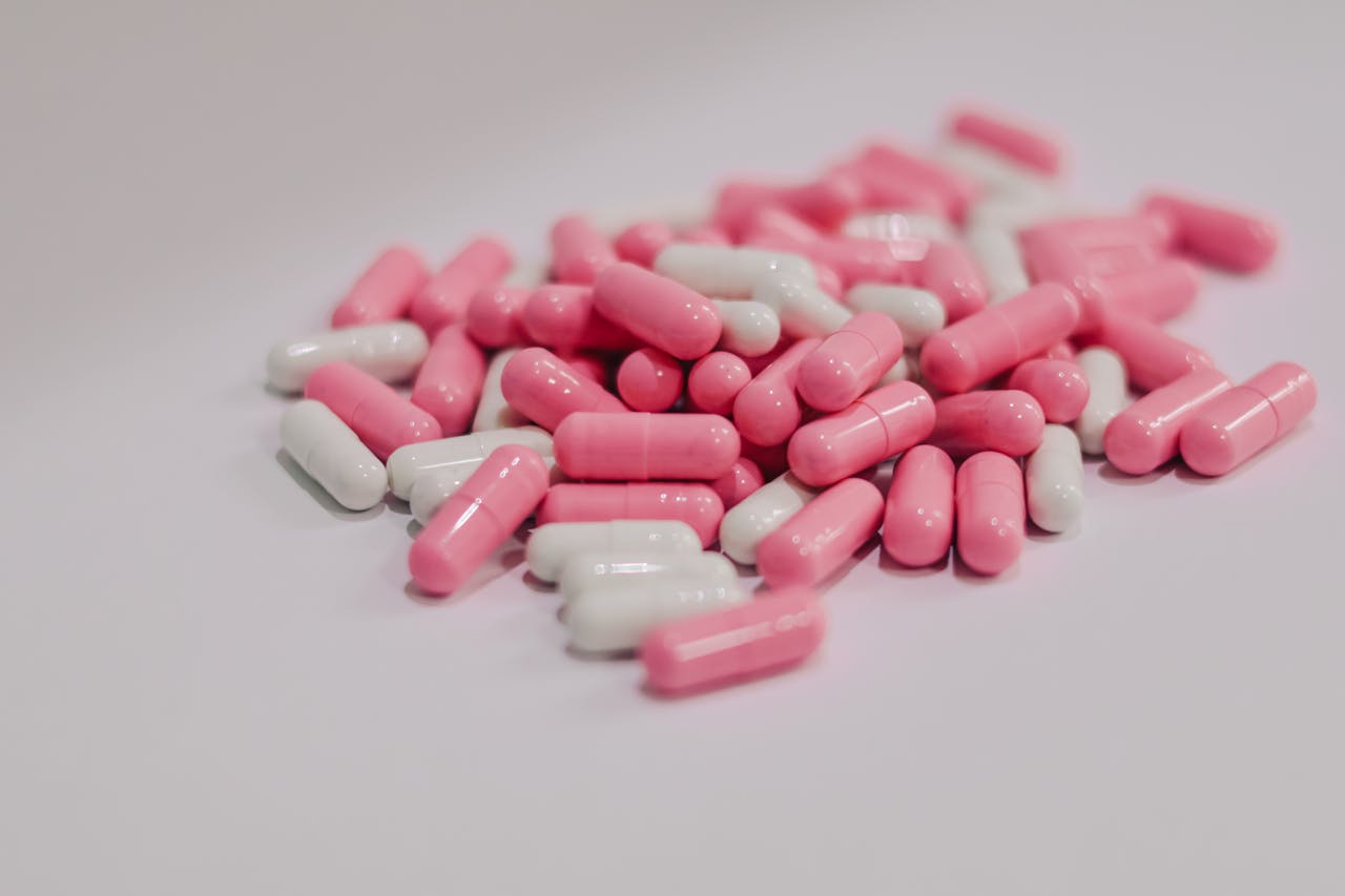 heros-img Close-up of pink and white pharmaceutical capsules scattered on a white surface.